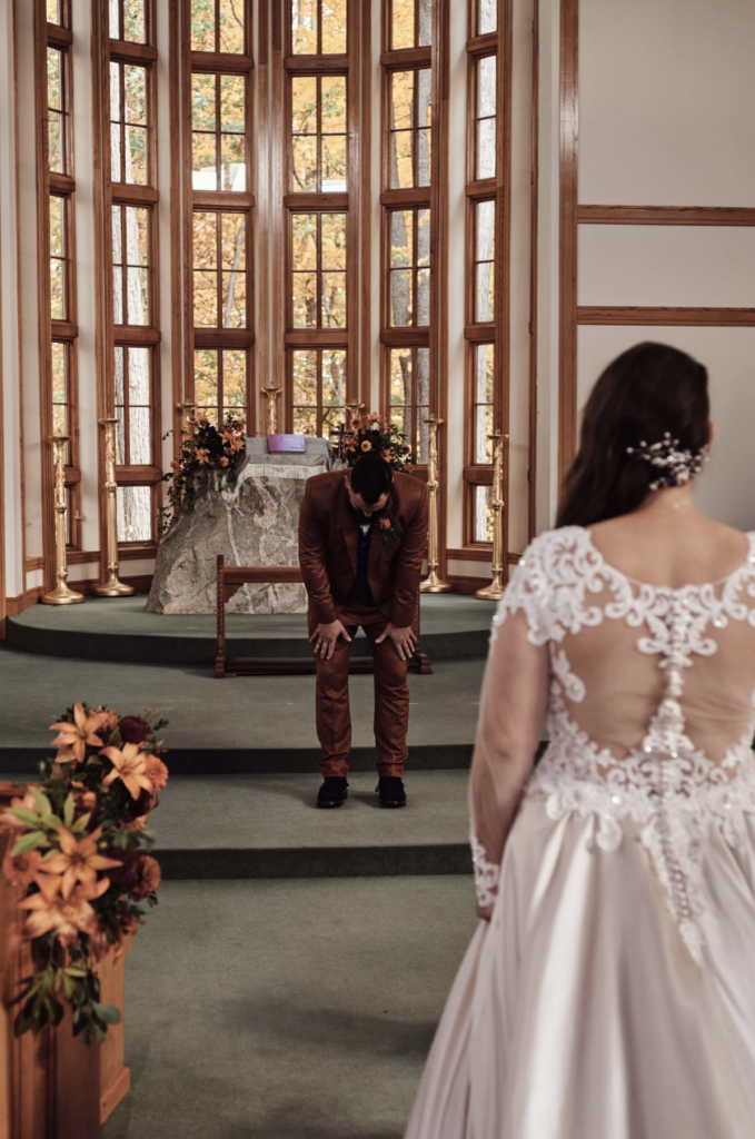 A groom is wrapped in emotion during his first look of his beautiful bride at a church in Rochester Hills, Michigan. Image by Erika Black Photography